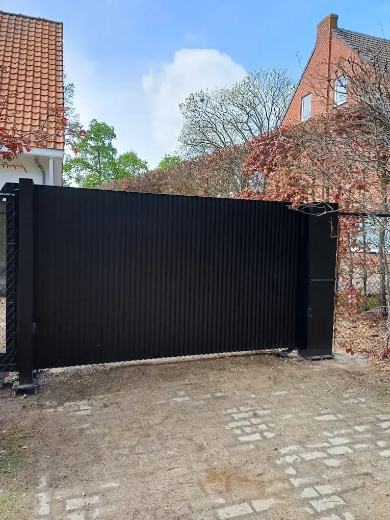 Zwarte schuifpoort met verticale lamellen en geïntegreerde loopdeur